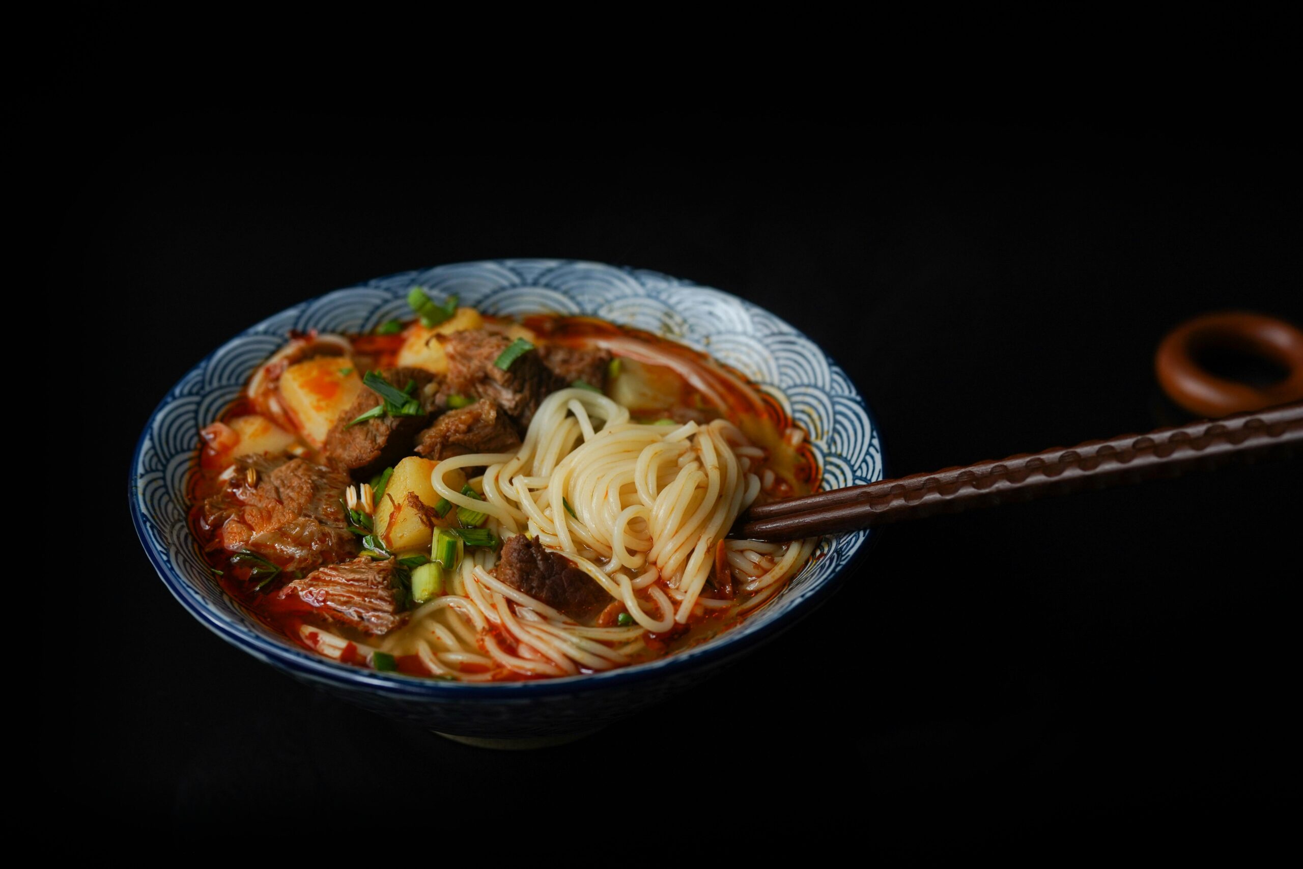 A savory bowl of Asian noodle soup with beef and vegetables, garnished with scallions.
