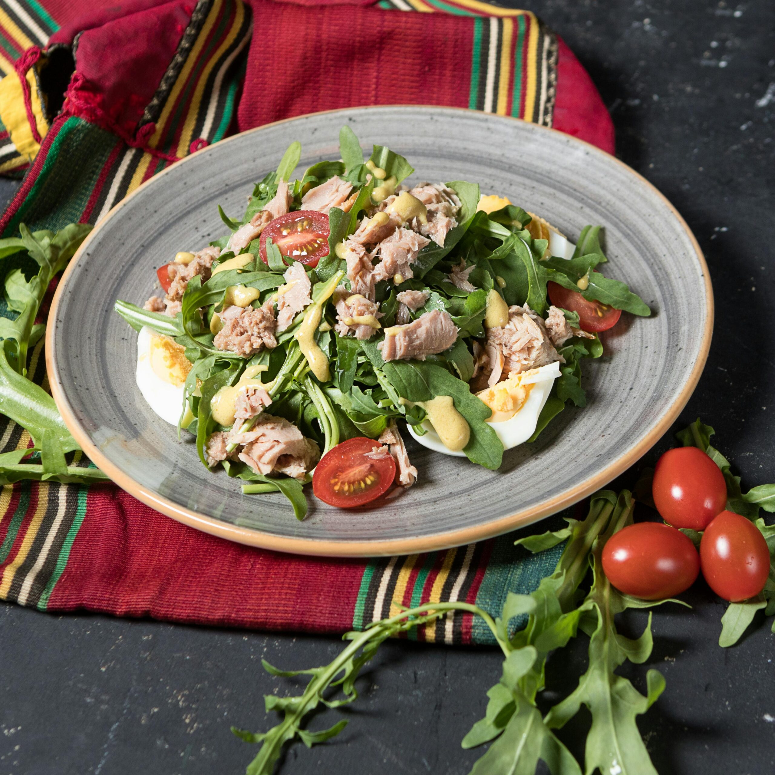 A delicious and healthy tuna salad with arugula, cherry tomatoes, and boiled eggs on a ceramic plate.